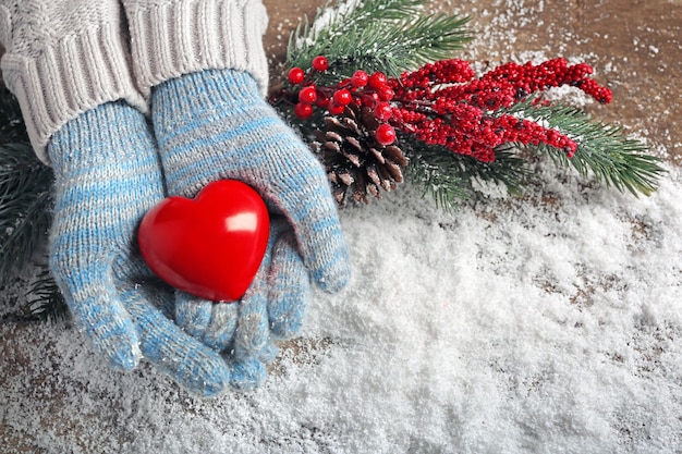 Женские руки в синих рукавицах с декоративным сердцем на фоне снега