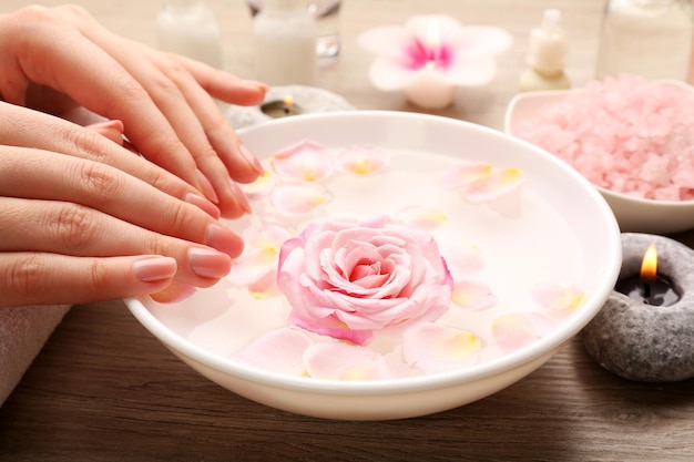 Female hands and bowl of spa water with flowers closeup