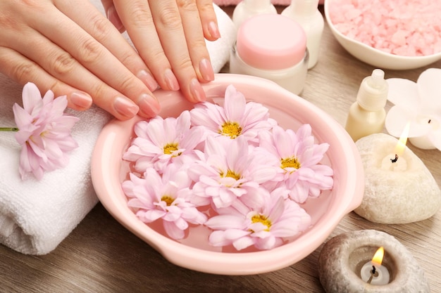 Female hands and bowl of spa water with flowers closeup