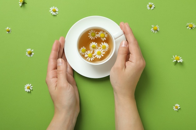 Female hands and chamomile tea on green