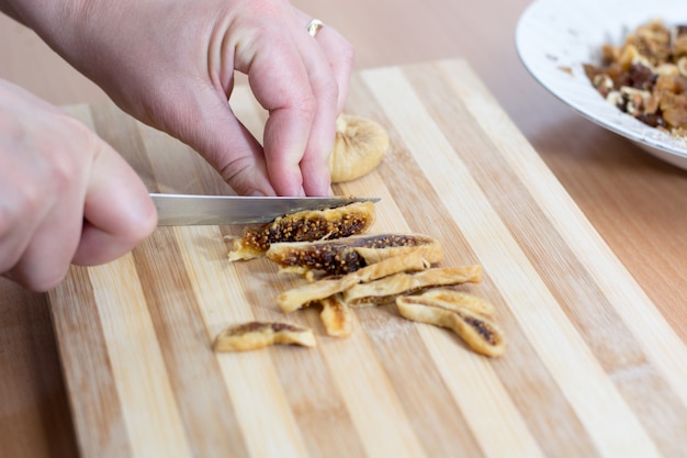 Mani femminili che tagliano il fico secco sul piatto di legno