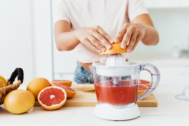 Mani femminili e spremiagrumi durante la preparazione del succo di pompelmo fresco