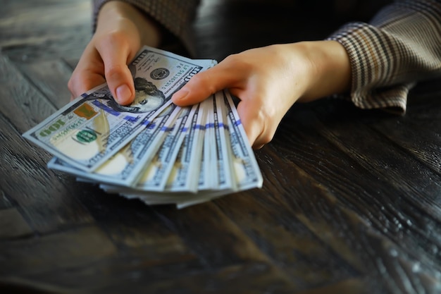 Female hands counting American one hundred dollar bills against the background of smaller bills of money lying on the table