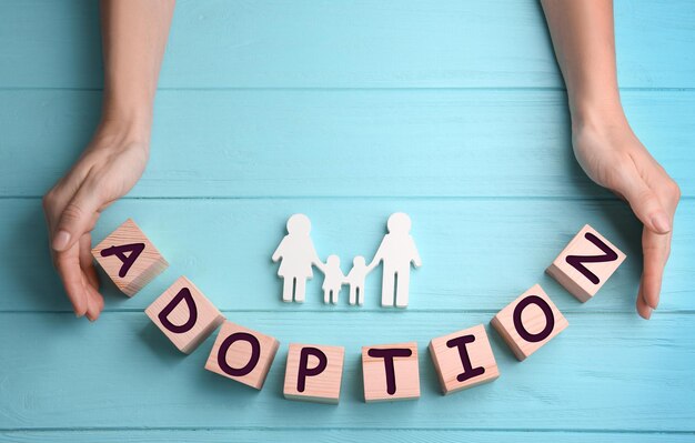 Photo female hands cubes with word adoption and figure in shape of happy family on wooden background