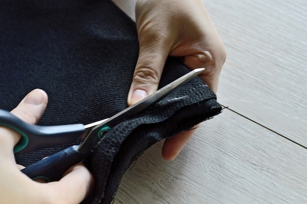 Female hands cut the black fabric with scissors. close-up.