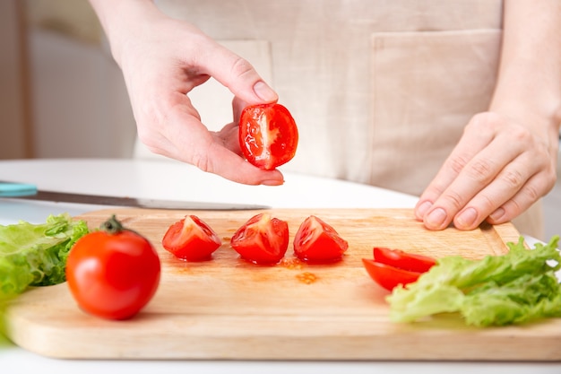 Female hands cut a juicy red tomato into quarters or slices with a knife on a wooden cutting board. A method of preparing vegetables and ingredients before cooking.