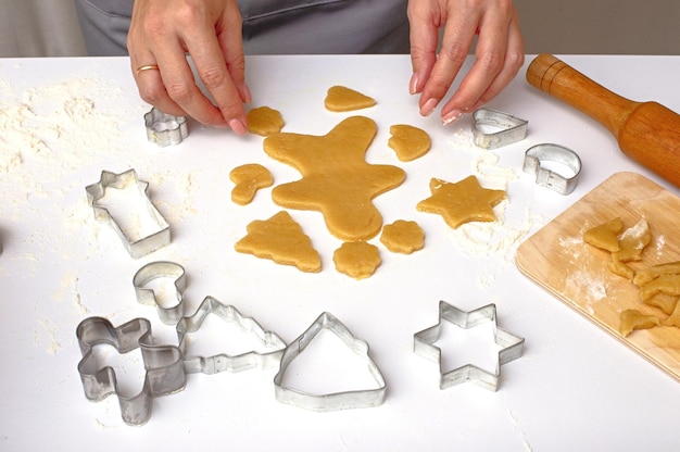 Female hands cut out christmas cookies from dough using metal molds on a white table