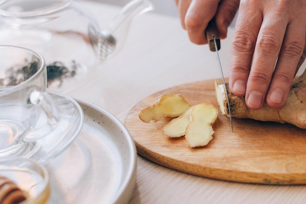 Female hands cuts fresh ginger on table Preparation of health tea antioxidant drink