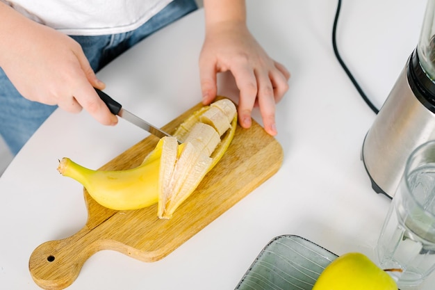 Foto mani femminili che tagliano la banana per la miscelazione di bevande primaverili vegane concetto di alimentazione consapevole dieta vista superiore