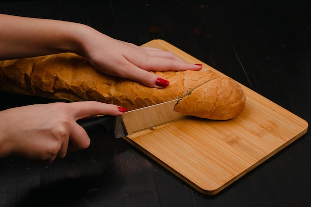 木材の背景にまな板でパンを切る女性の手