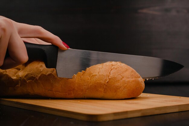 木材の背景にまな板でパンを切る女性の手