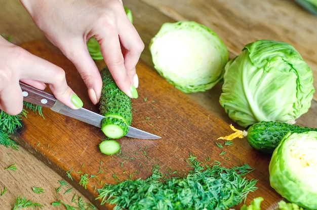 Photo female hands cutting fresh green cucumbers on a wooden cutting board