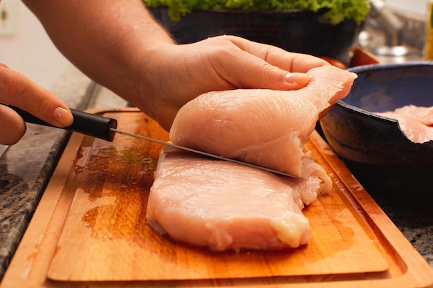 Female Hands Cutting Raw Chicken Breast on Wooden Cutting Board