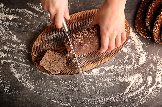 Female hands cutting rye bread with seeds on grey table background