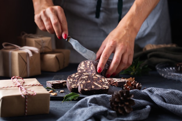 伝統的なイタリアのデザートクリスマスチョコレートサラミを切る女性の手