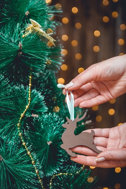 Female hands decorate Christmas tree with wooden Christmas decoration