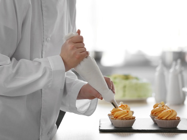 Female hands decorating tarts with cream.