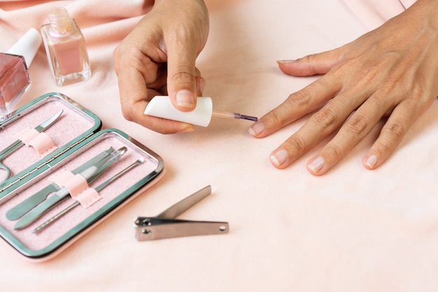 Mani femminili facendo smalto in colore rosa perla con set di strumenti per manicure e strumenti su velluto di seta rosa. bellezza, concetto di manicure