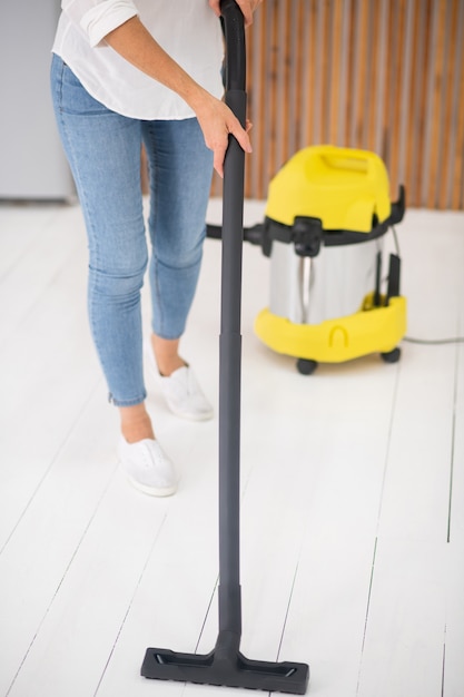 Female hands easily vacuuming floor holding black tube of modern vacuum cleaner