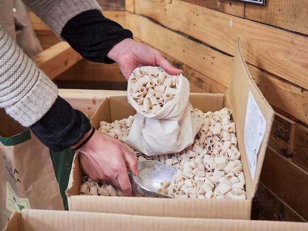 Female hands filling cloth bag with raw pasta, buying in bulk