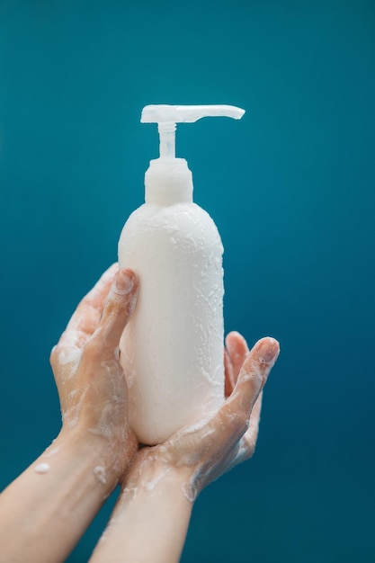 Female hands in foam with white plastic pump bottle on blue background