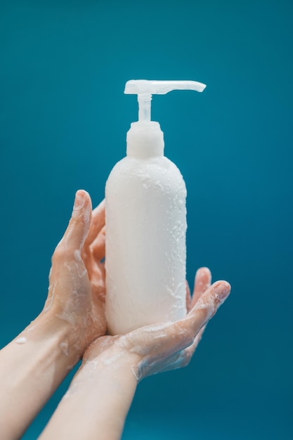 Photo female hands in foam with white plastic pump bottle on blue background