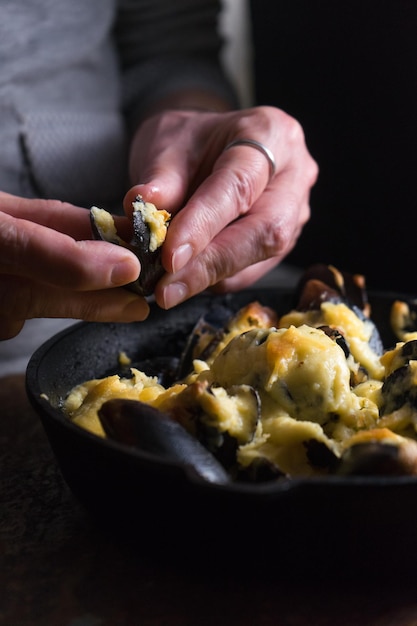 Female hands over a frying pan with mussels under cheese sauce