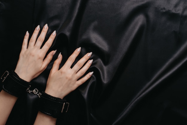 Female hands in handcuffs on a dark silk sheet