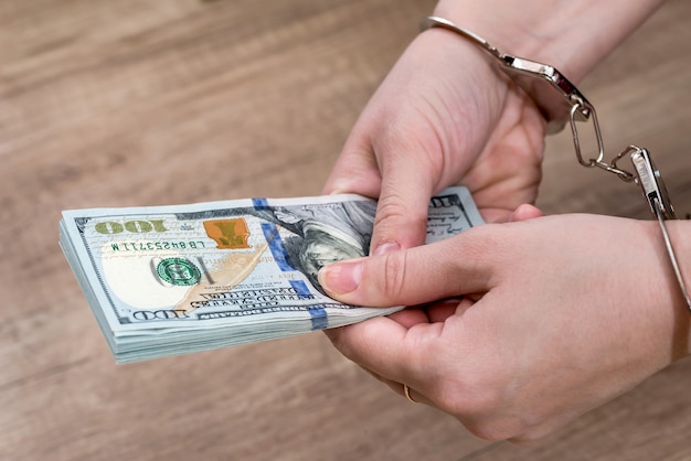 Female hands in handcuffs with dollars on the table