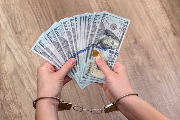 Female hands in handcuffs with dollars on the table