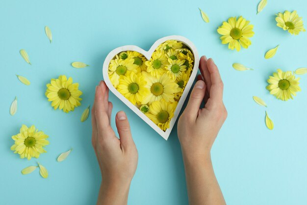 Mani femminili e cuore con crisantemi su sfondo blu.