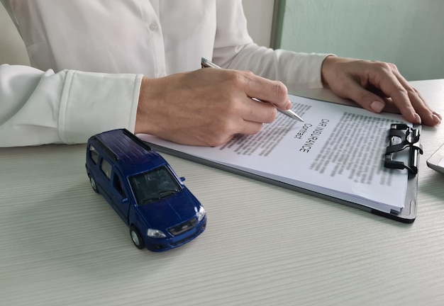 Female hands hold ballpoint pen over car insurance blank and toy car