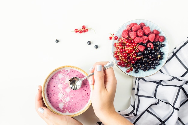 Female hands hold a berry smoothie in a bowl next to a plate with raspberries