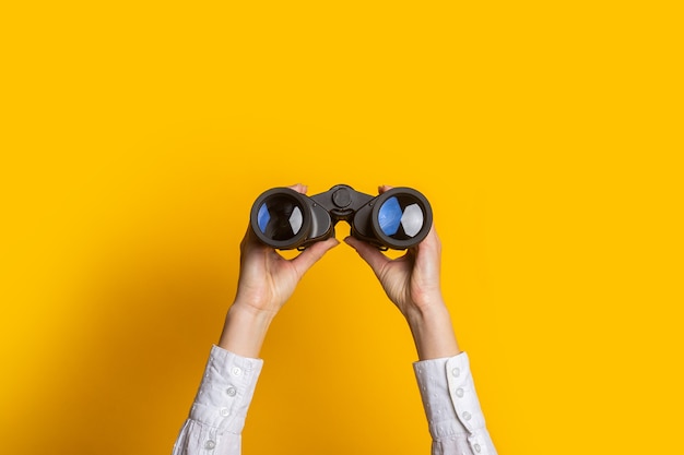Photo female hands hold black binoculars on a bright yellow background