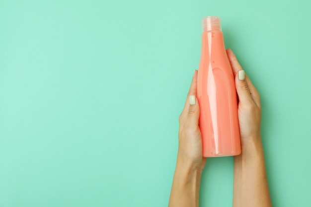 Female hands hold blank bottle of shampoo on mint