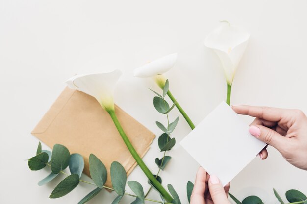 写真 女性の手は、花の上に空白の白いシートを保持します。上面図。モックアップ