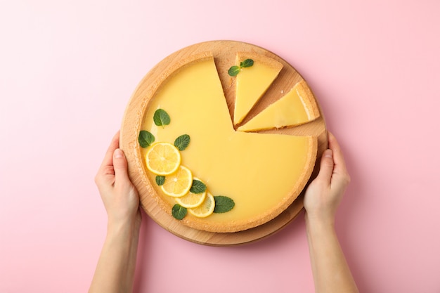 Female hands hold board with lemon tart on pink background, top view