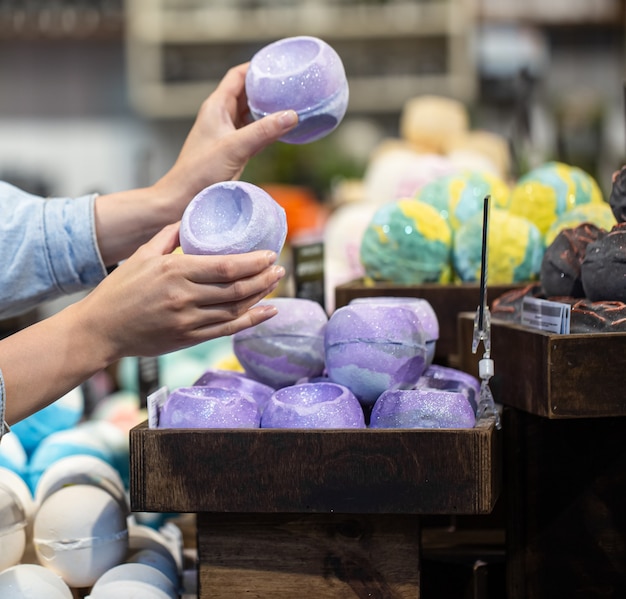 Mani femminili tengono bombe da bagno luminose in un negozio di cosmetici. concetto di cura del corpo.