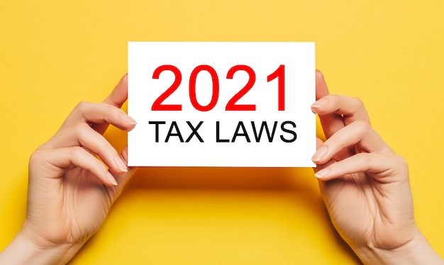 Female hands hold card paper with text 2021 tax laws on a yellow background. Business and finance concept