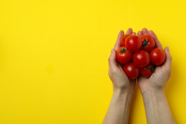 Foto mani femminili tengono pomodorini su sfondo giallo