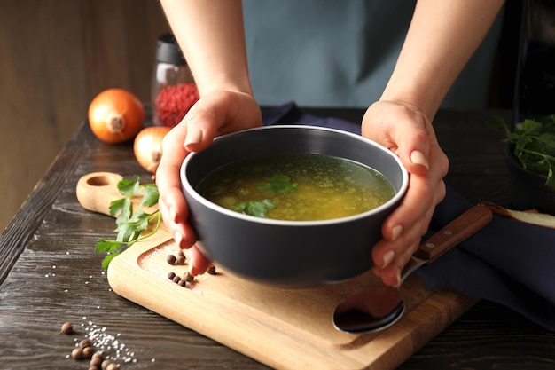 Female hands hold chicken soup or broth on a wooden table