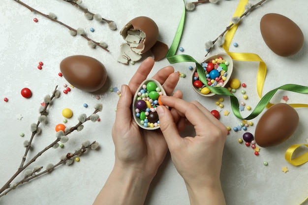 Female hands hold chocolate egg on white textured wall with Easter accessories