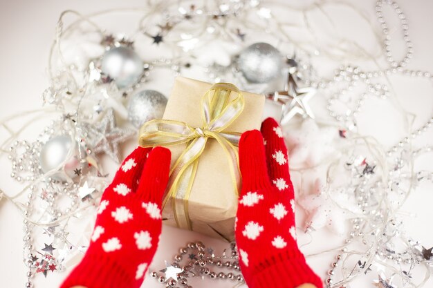 Female hands hold a Christmas gift with a gold ribbon in red mittens, new year mood, preparation for the celebration. View from above.