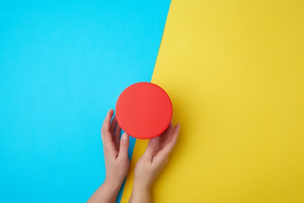 Foto le mani femminili tengono una scatola di cartone di carta chiusa su un giallo-blu