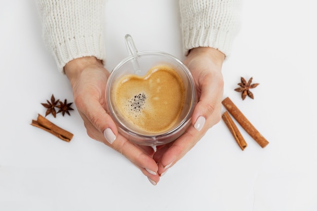 Female hands hold a cup of coffee in the shape of a heart. Cinnamon and star anise. Top view.