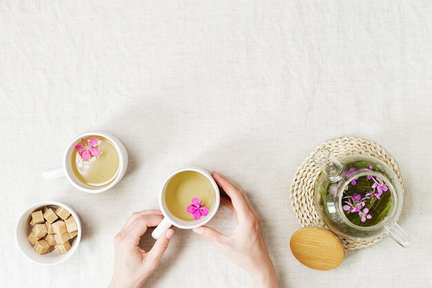 Female hands hold cup with fireweed tea transparent glass teapot herbal hot tea from