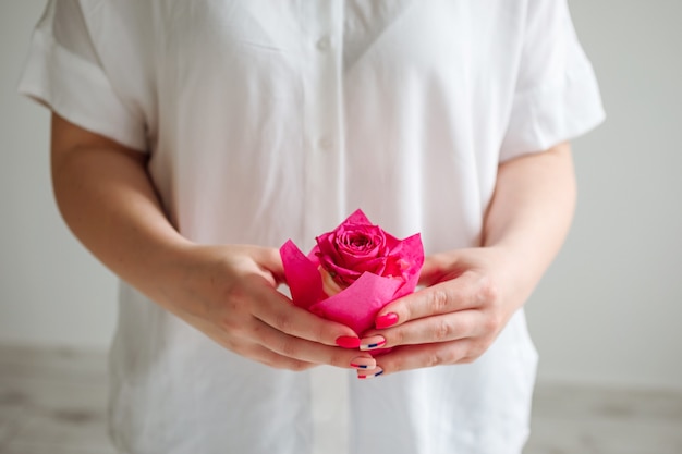 Female hands hold cupcake decorated with rose bud in front of the white shirt.