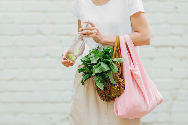 女性の手は、野菜、野菜、再利用可能な水筒のエコバッグを持っています。ゼロウェイスト。持続可能なライフスタイルのコンセプト。