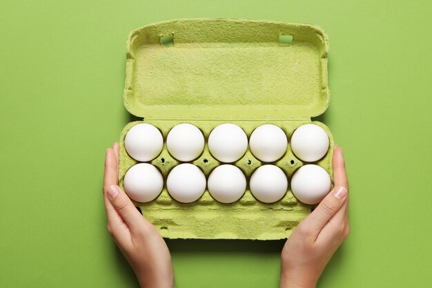 Foto le mani femminili tengono la scatola delle uova su sfondo verde