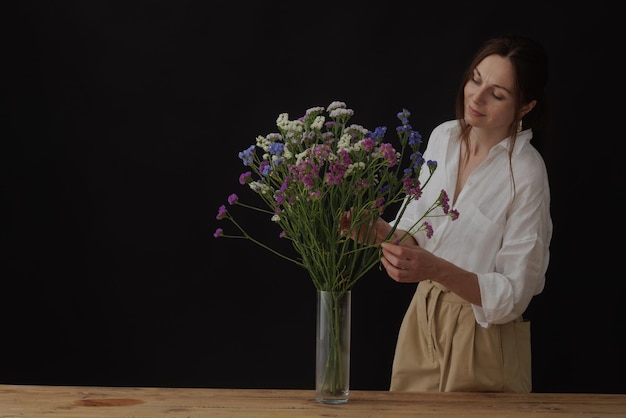 女性の手は、木製のテーブルの暗い背景のモックアップにガラスの花瓶にユーカリを保持します